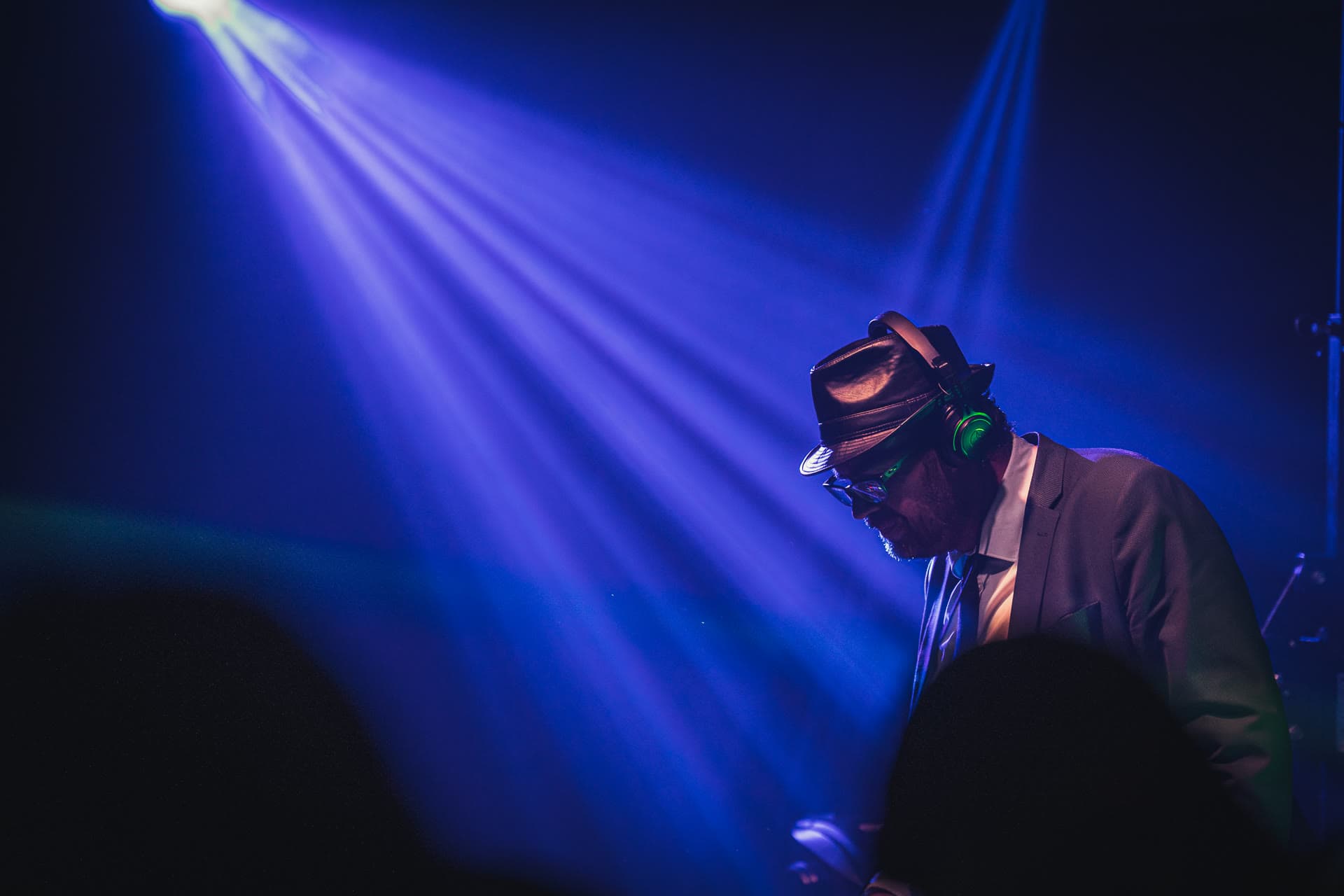 Julien Bonhomme de profil derrière ses platines, chapeau et lunettes, éclairé par un unique faisceau bleu dans une salle plongée dans le noir.